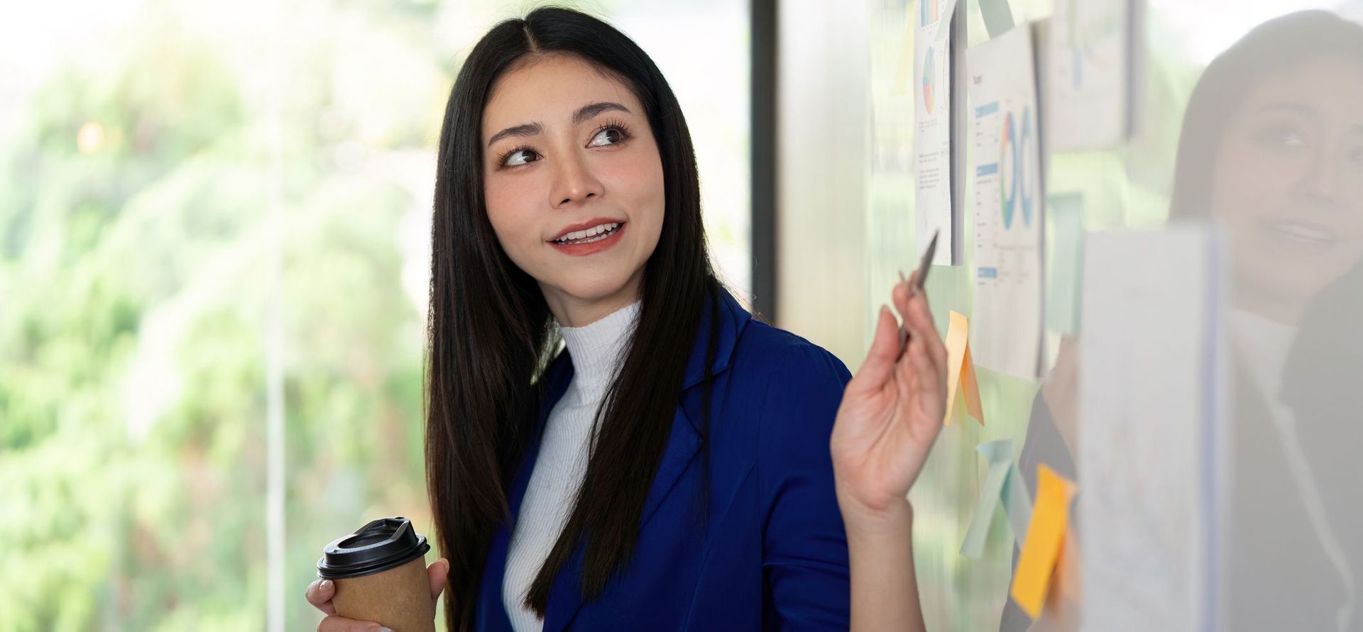 female businesswoman points to whiteboard while holding coffee cup